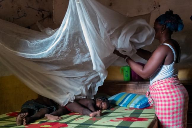 Camara, a 21 years old mother of 2 children, is installing over her bed the mosquito net she received when she was pregnant from her first child.